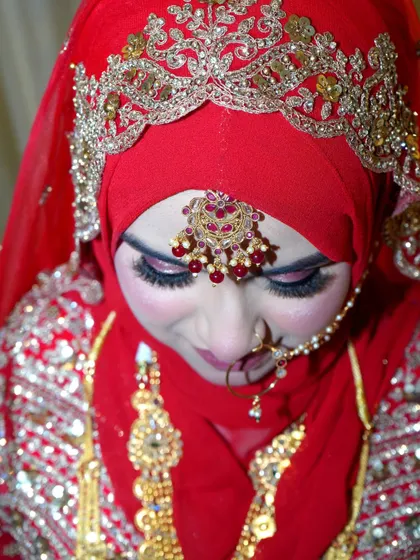 A close-up of a Muslim bride in her stunning red and gold attire, looking down with a gentle smile.