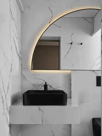 In the guest bathroom, we used a dramatic arched mirror with backlighting to create a focal point. The black vessel sink and matte black fixtures provide a sharp, modern contrast against the white marble walls.