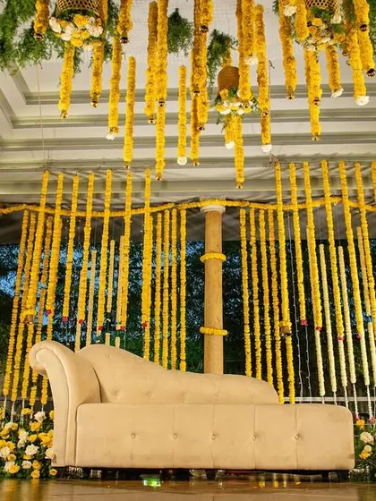 A full view of a Haldi stage setup, heavily decorated with strings of marigold flowers (genda phool). The design creates a traditional and immersive environment for the ceremony.