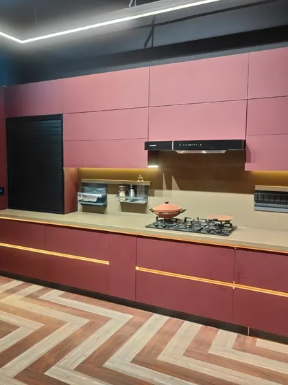 This wide shot captures the beautiful balance of color and texture in this contemporary kitchen. The warm wood flooring in a chevron pattern complements the bold magenta cabinets, creating a space that is both daring and harmonious.