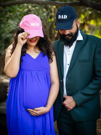 A fun and playful shot using 'Mom' and 'Dad' caps. This outdoor maternity photo captures the couple's excitement and personality as they look forward to becoming parents.