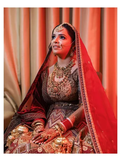 A seated portrait of the bride, looking regal in her richly detailed lehenga. The warm, soft lighting adds to the classic and elegant feel of the photograph.