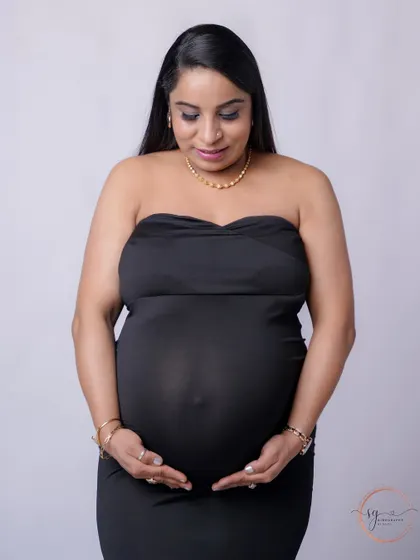 A simple and heartfelt solo portrait. The mom-to-be looks down at her bump with love, captured against a clean, minimalist background.