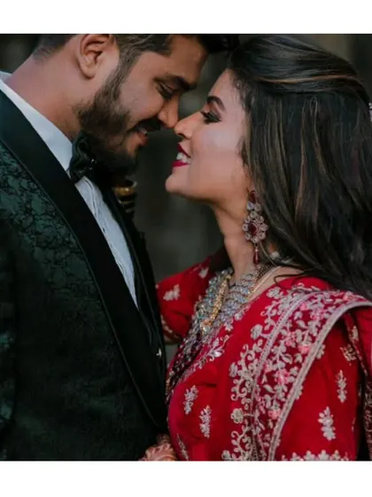 A close-up shot capturing the romance. The groom's dark green tuxedo and the bride's traditional red lehenga create a rich, cinematic look for any wedding album.