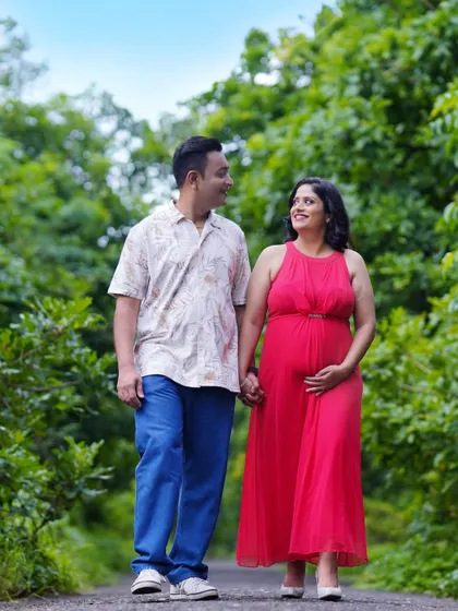 A relaxed photo of an expecting couple walking hand-in-hand through a park. The natural green surroundings provide a calm and beautiful backdrop for their maternity session.