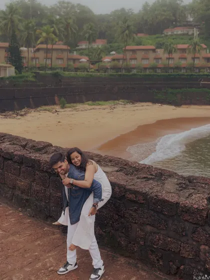 A playful piggyback ride along the historic fort walls overlooking a Goan beach. This candid moment is full of laughter and shows the fun side of a destination pre-wedding shoot.