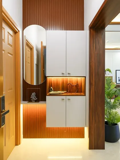 A warm and inviting foyer design with a floating shoe cabinet featuring an illuminated niche, set against a backdrop of fluted wooden panels that guide you into the living space.
