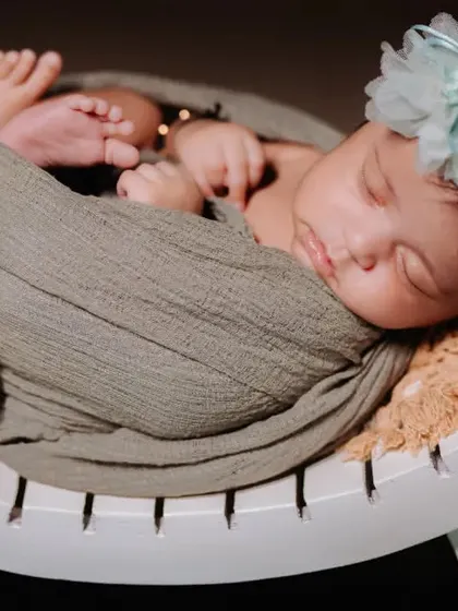 A serene newborn portrait, beautifully swaddled and resting on a curved white bench. The soft green tones create a peaceful and natural look.