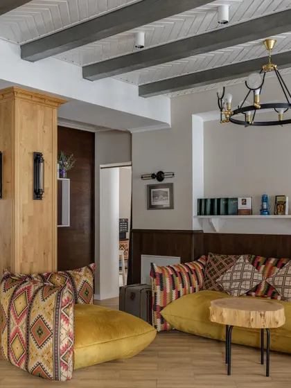 A cozy lounge area with a rustic, cabin-like feel. The space features low-slung yellow sofas with geometric-patterned cushions and a natural wood slice coffee table.