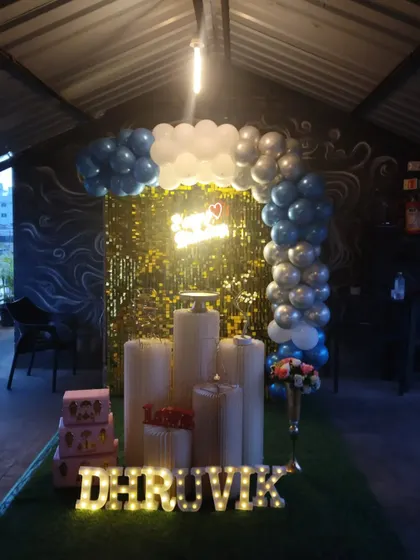 A cozy birthday setup in a cafe, with a balloon arch over a golden sequin backdrop and marquee letters.