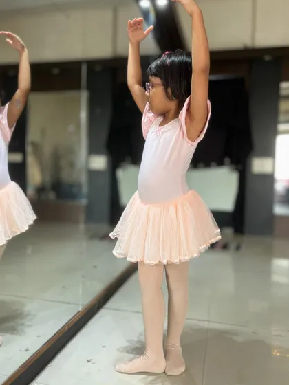 A young student practices her poses in a pink leotard and tutu. Proper attire is encouraged in my ballet classes to help with movement and discipline.