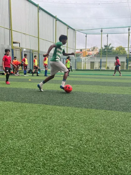 A player in a green and white kit dribbles a red ball, focusing on close control during a training exercise.