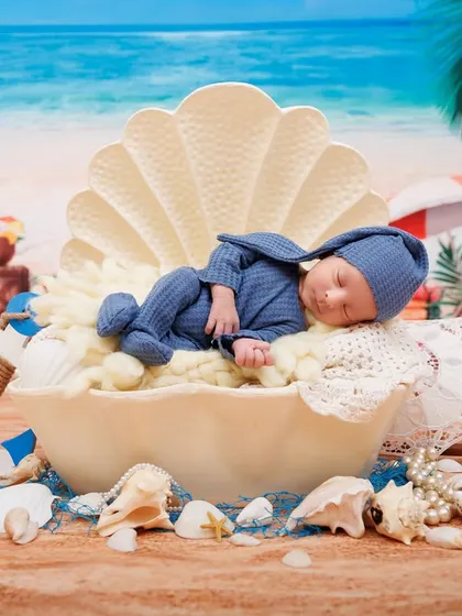 A wide shot of the 'pearl in a shell' newborn setup, with a beach backdrop and nautical props. A creative and beautiful way to announce a new arrival.