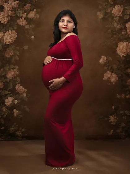 Standing against a beautiful floral backdrop, this mother-to-be in a classic red gown is the picture of elegance. The painted background adds a layer of artistry to the portrait.