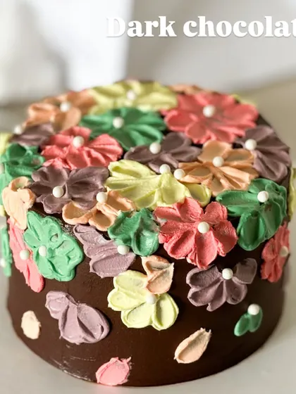 A dark chocolate cake covered in a garden of colorful, hand-piped flowers. This design shows that even a rich chocolate cake can be bright and whimsical.
