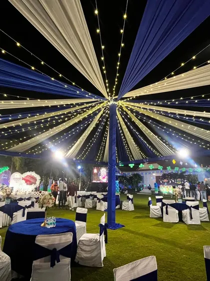 An outdoor evening event with a stunning canopy of blue and white drapes. The entire tent is illuminated with strings of fairy lights, creating a starry night effect over the guest seating area.