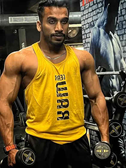 A front-facing pose holding dumbbells. This shot highlights the shoulder and bicep definition that forms the foundation of a classic men's physique look.