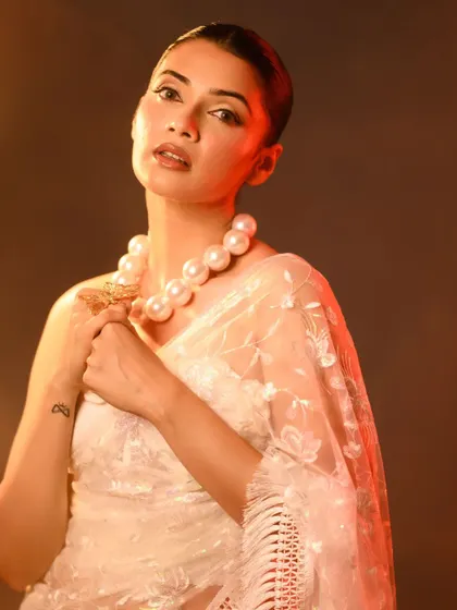A close-up version of the previous shot, focusing on the subject's expression and the large pearl necklace. The warm lighting adds a soft, glamorous glow.