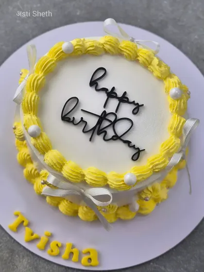 A simple yet cheerful yellow birthday cake with piped borders and delicate ribbon bows.