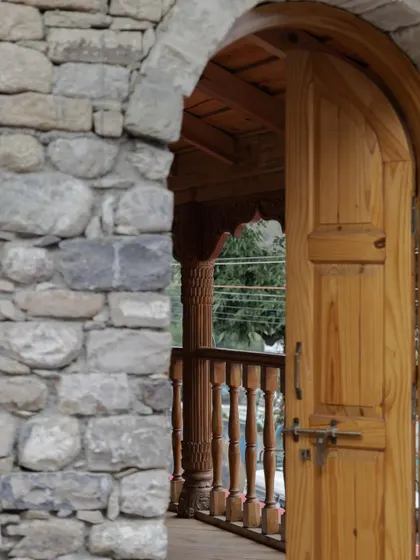 A glimpse from the stone entryway to the wooden balcony, showing the seamless transition between the robust, historic structure and the finely crafted details.