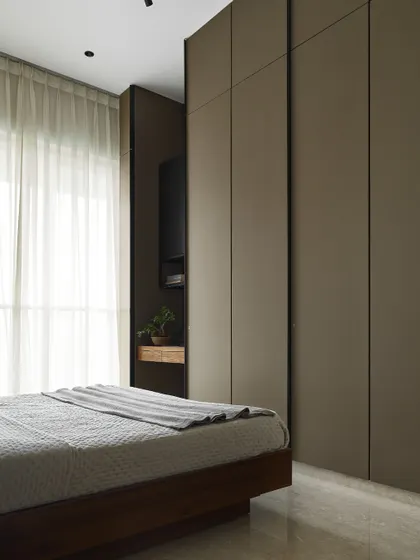 This view of the Taupe Bedroom shows the seamless integration of the wardrobe and a small niche for a television. The consistent use of a muted, earthy tone on the cabinetry creates a cohesive and calming effect.