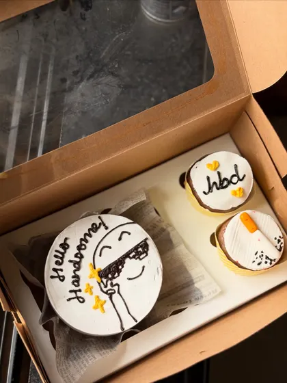 A cool and fun birthday set with a "Hello Handsome!" bento cake featuring a cartoon character in sunglasses. The two accompanying cupcakes are also decorated with fun, simple designs.