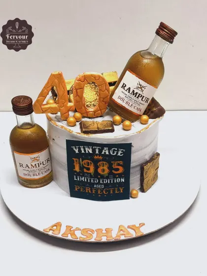 A vintage-themed cake for a 40th birthday, featuring Rampur Double Cask whisky miniatures. The "Vintage 1985" edible print adds a personalized touch.