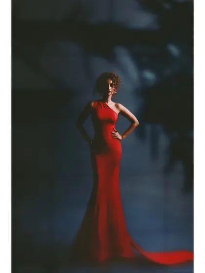 A classic studio shot of a woman in red. The styling is pure Hollywood glamour, with a figure-hugging red gown and a powerful stance against a moody, textured background.