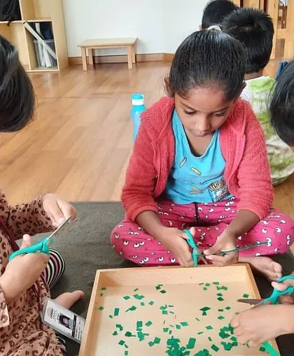 Developing scissor skills is a key part of our practical life curriculum. Here, children are practicing cutting with focus and precision, an activity that builds hand strength and coordination for writing later on.