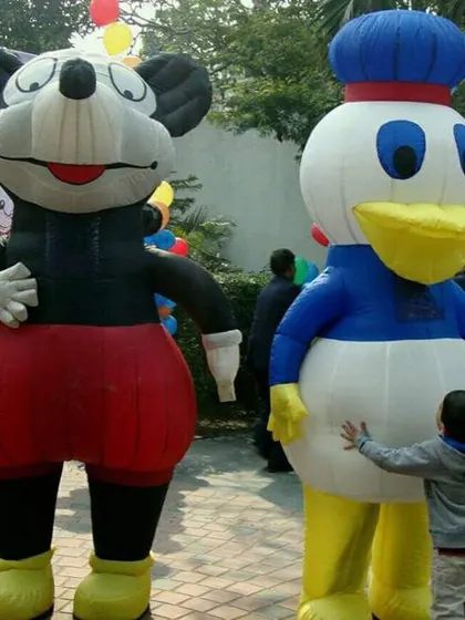 A child gives a hug to a giant inflatable Donald Duck next to Mickey Mouse. These large characters are very popular for photos.