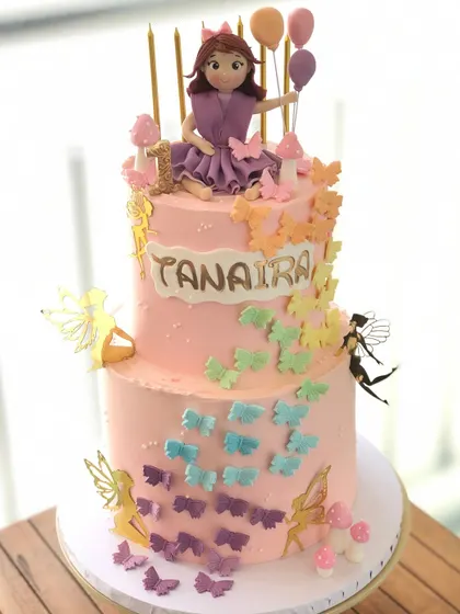 A two-tiered fairy and butterfly cake for a magical first birthday. This cake is adorned with a cascade of colorful butterflies and whimsical fairy figures.