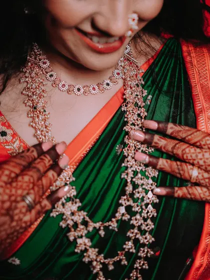 A close-up shot that puts the focus on the bride's magnificent layered necklaces and her dark green saree. This highlights the beauty and craftsmanship of traditional wedding jewellery.