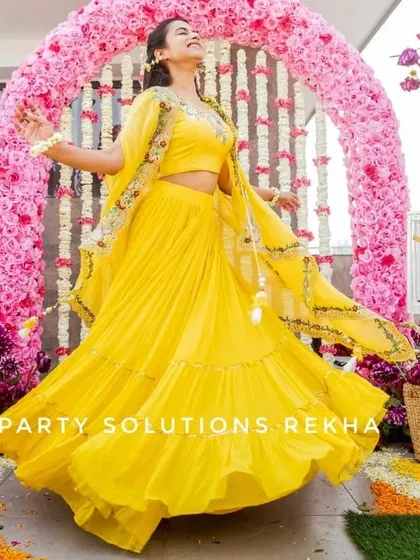 A joyful bride twirling in her yellow lehenga. The backdrop of a pink floral arch and hanging jasmine strings makes for a perfect, celebratory photo from her Haldi ceremony.