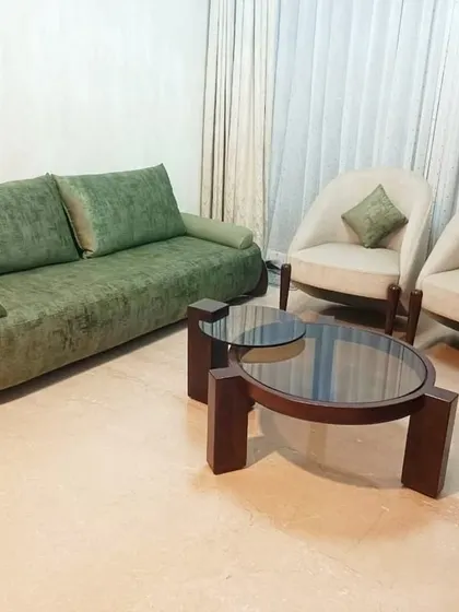 This living room set, featuring a green three-seater sofa and two cream-colored accent chairs, creates a balanced and inviting atmosphere. The simple, clean lines of the furniture are complemented by a modern multi-level center table.