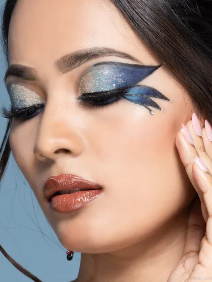 A creative beauty portrait featuring graphic blue and silver winged eyeliner. The focus is entirely on the makeup artistry, making it a powerful image for a beauty campaign.