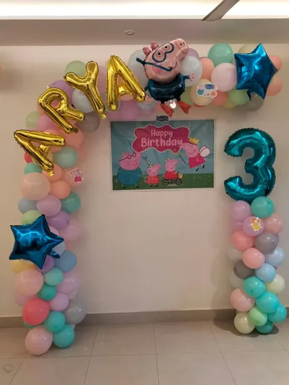 A Peppa Pig themed balloon arch in pastel colors for a 3rd birthday, complete with a character backdrop and foil name balloons.