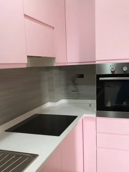 A work-in-progress shot of a pink kitchen, showing the installation of a built-in oven. The high-gloss pink finish creates a playful yet stylish atmosphere.