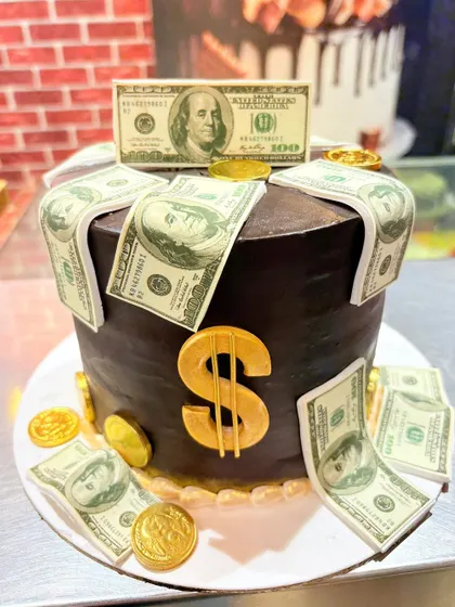 A rich chocolate cake overflowing with edible dollar bills and gold coins.