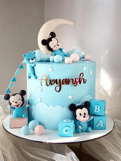 A dreamy Mickey Mouse cake for a baby's celebration. This design uses a soft blue color palette and features a sleeping Mickey on a crescent moon.