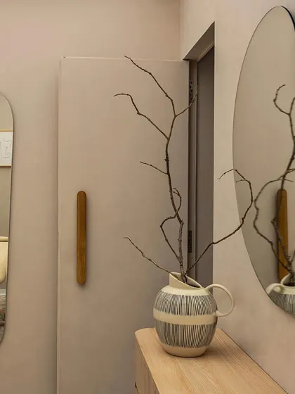 A closer look at the vanity area shows the custom details that define this project. The amoebic mirror, wooden door pull, and ceramic vase with dried branches come together to create a composition that feels both natural and artfully curated.