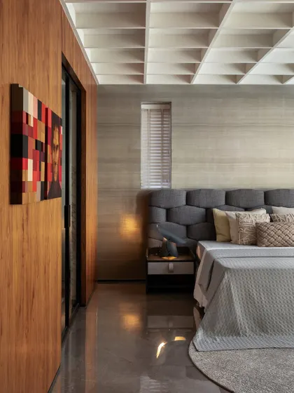 This master bedroom exudes sophistication with its rich wood tones and coffered ceiling. The tufted grey headboard and colorful artwork add layers of texture and personality, creating a perfect mix of comfort and style.