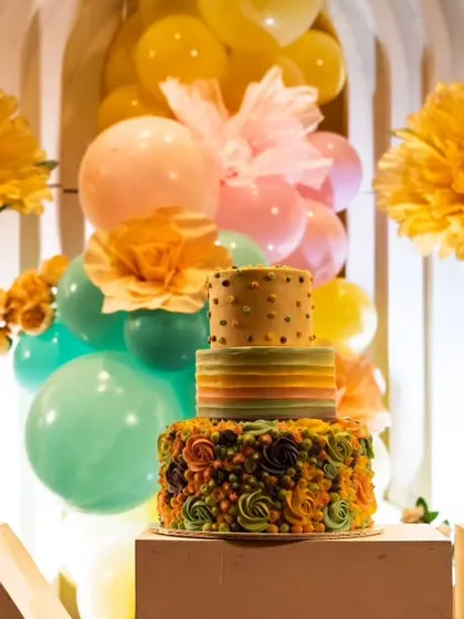 A close-up on the colorful cake for the floral garden theme. The cake itself becomes a part of the decor, perfectly matching the rainbow aesthetic of the balloons and flowers.