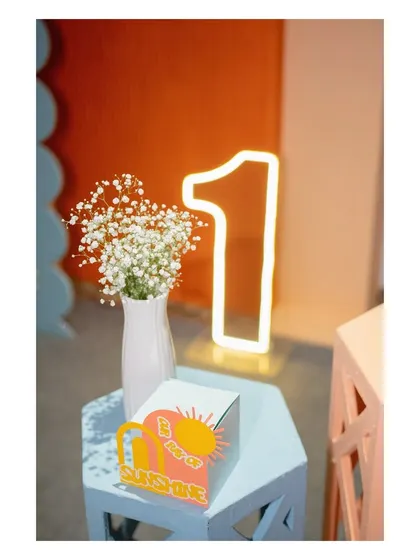 A close-up of a 'You Are My Sunshine' favor box and a light-up '1' sign, showing the thoughtful details of the party.