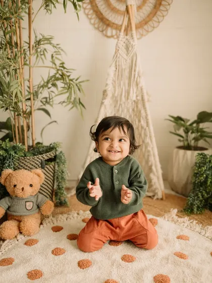 A little boy clapping his hands with a huge smile, surrounded by the natural textures of the studio setup.