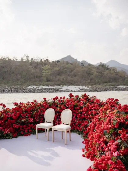 A simple yet powerful setup for the couple, with two elegant chairs placed before a wall of vibrant red roses, overlooking the Ganges river. This design is all about making a statement with color and nature.