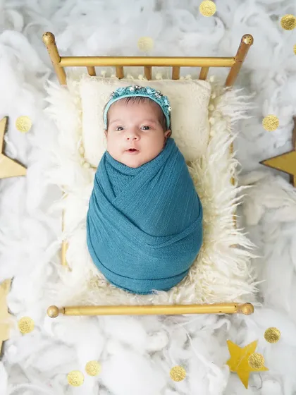Twinkle, twinkle, little star. This baby girl, wrapped in a blue swaddle, looks up with wide-eyed wonder from her tiny bed amidst clouds and stars.