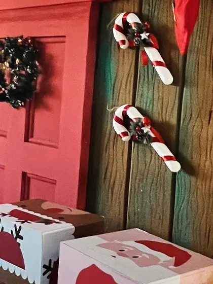 Candy cane props and a mini wreath on a red door, part of a larger Christmas scene.