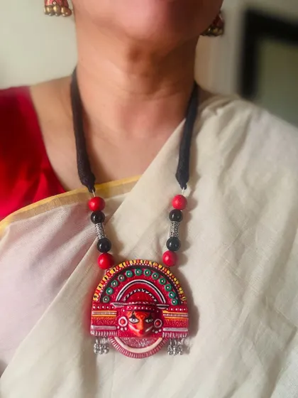 Here is the Theyyam-inspired terracotta pendant being worn. It sits beautifully against the simple elegance of an off-white saree, making the colors truly stand out.