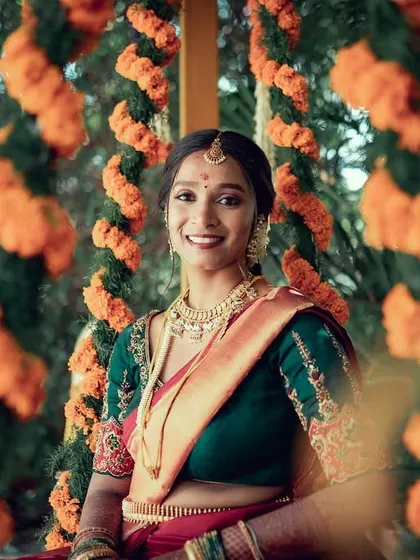 A beautiful bride smiling, framed by garlands of orange marigolds. The natural setting and traditional decor create a warm and festive atmosphere for this lovely wedding portrait.