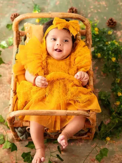 A beautiful portrait of a baby girl in a stunning yellow dress, set against a rustic, nature-inspired backdrop.